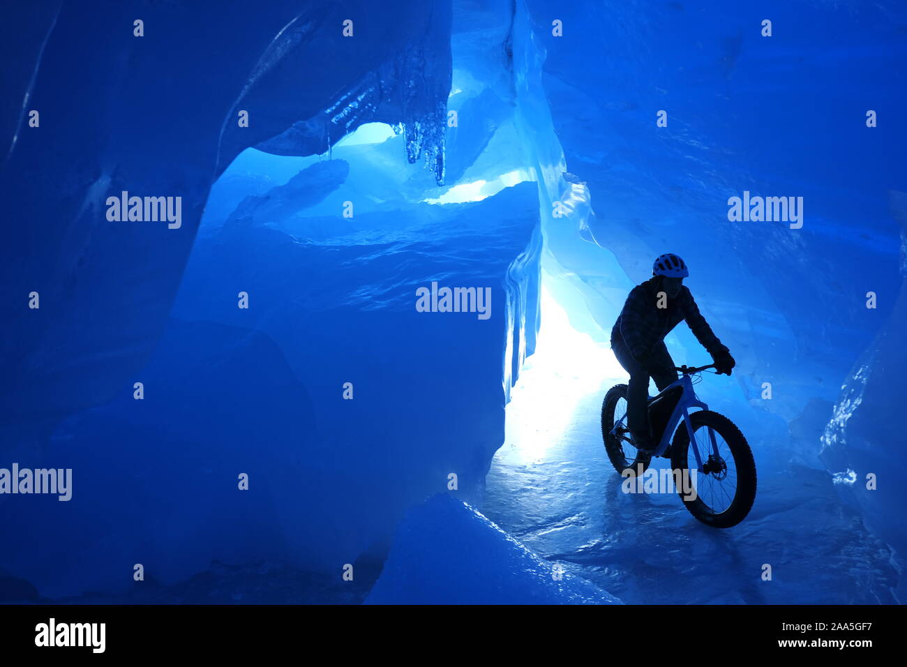 Man riding a fat tire snow bike inside a blue ice cave in an Alaska glacier. Stock Photo
