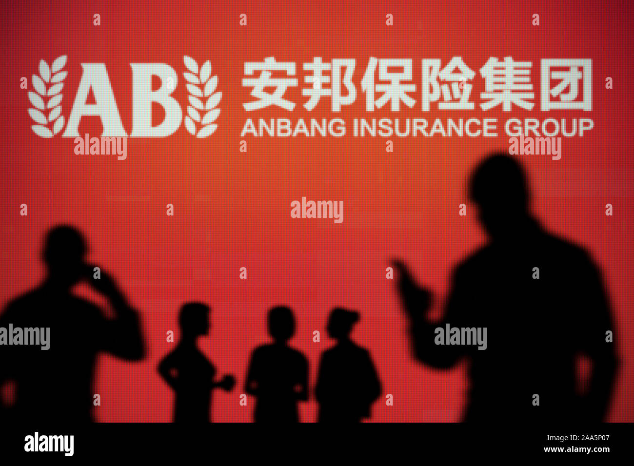 The Anbang Insurance Group logo is seen on an LED screen in the background while a silhouetted person uses a smartphone (Editorial use only) Stock Photo