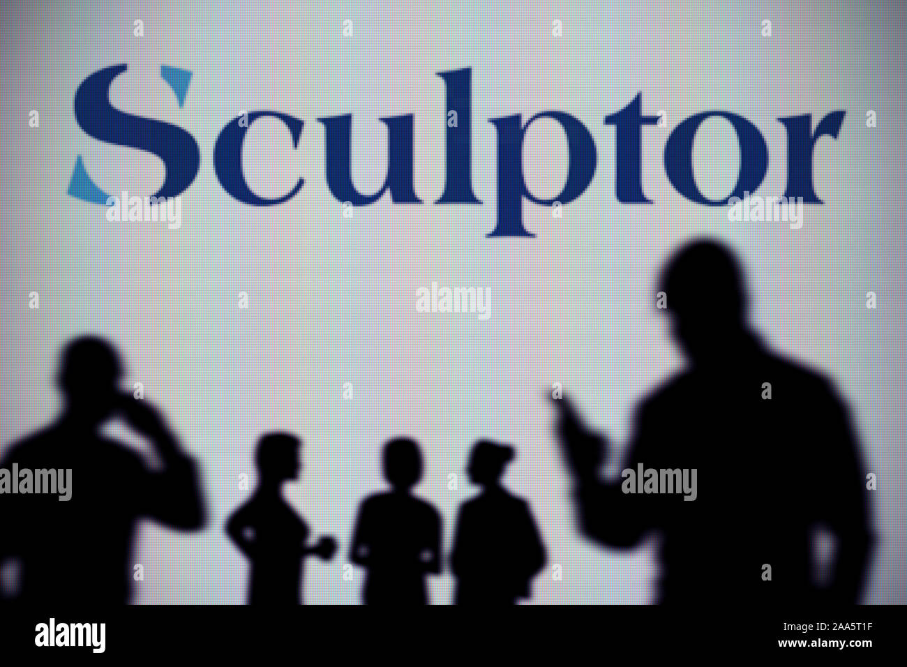 The Sculptor Capital Management logo is seen on an LED screen in the background while a silhouetted person uses a smartphone (Editorial use only) Stock Photo