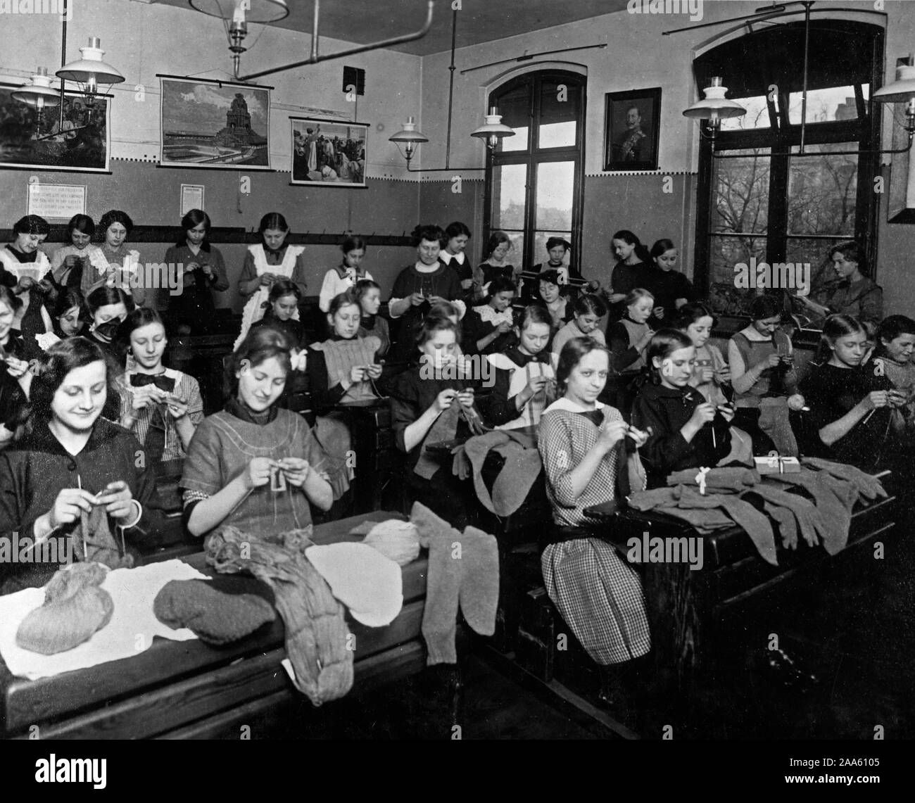 School children in domestic science classes learning to knit socks for the soldiers in the field. Good propaganda picture. Note Kaiser between biblical subjects on the wall ca. 1918 Stock Photo