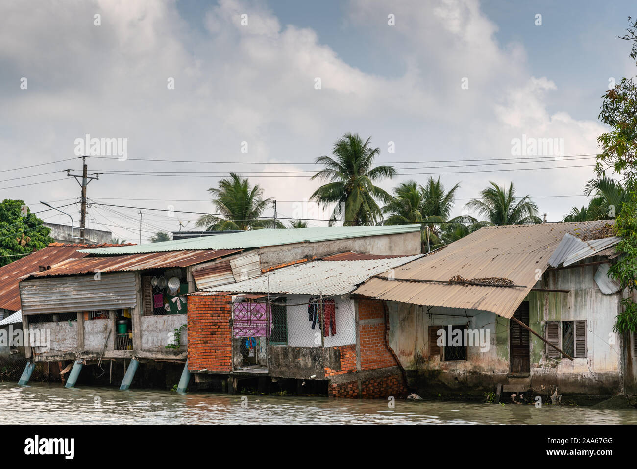 Cai Be, Mekong Delta, Vietnam - March 13, 2019: Along Kinh 28 canal. Row of slum-like poor houses built on stilts and on shore with corrugated roof pl Stock Photo
