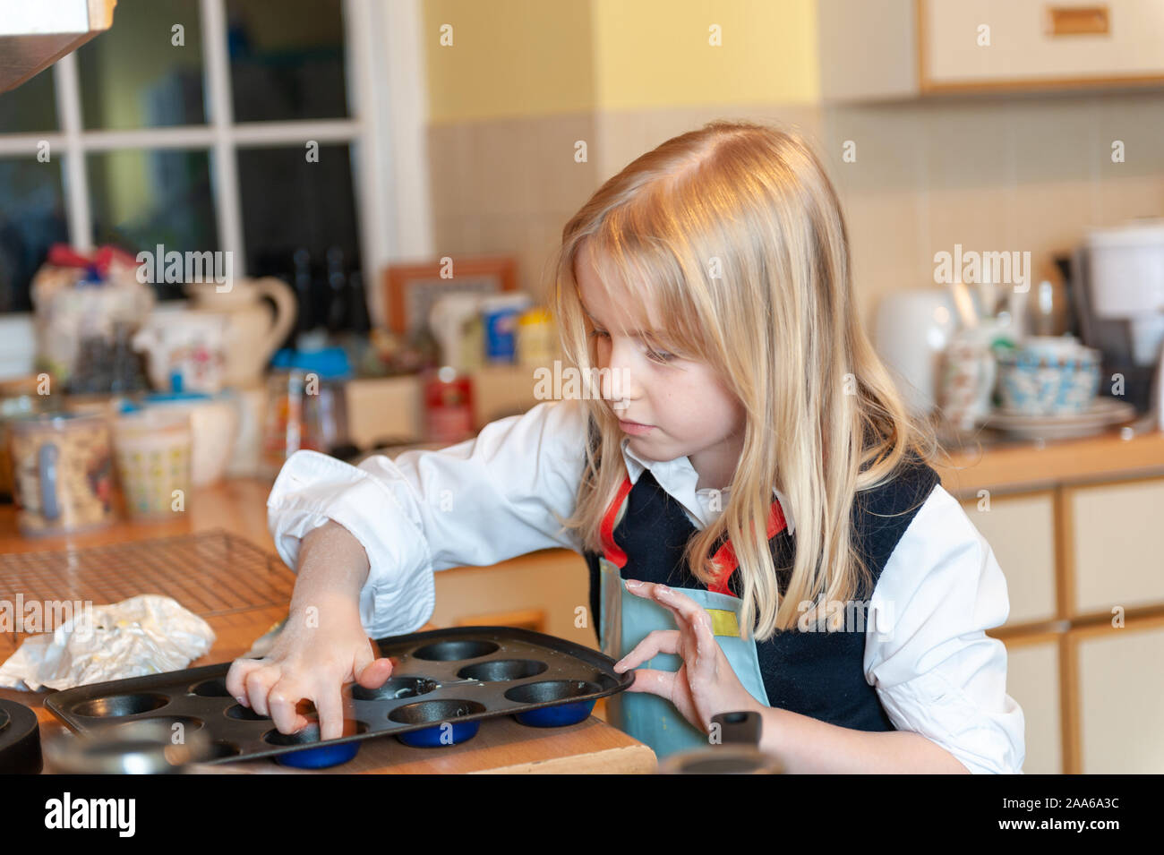 Pretty young blonde girl preparing to bake in a messy kitchen Stock Photo