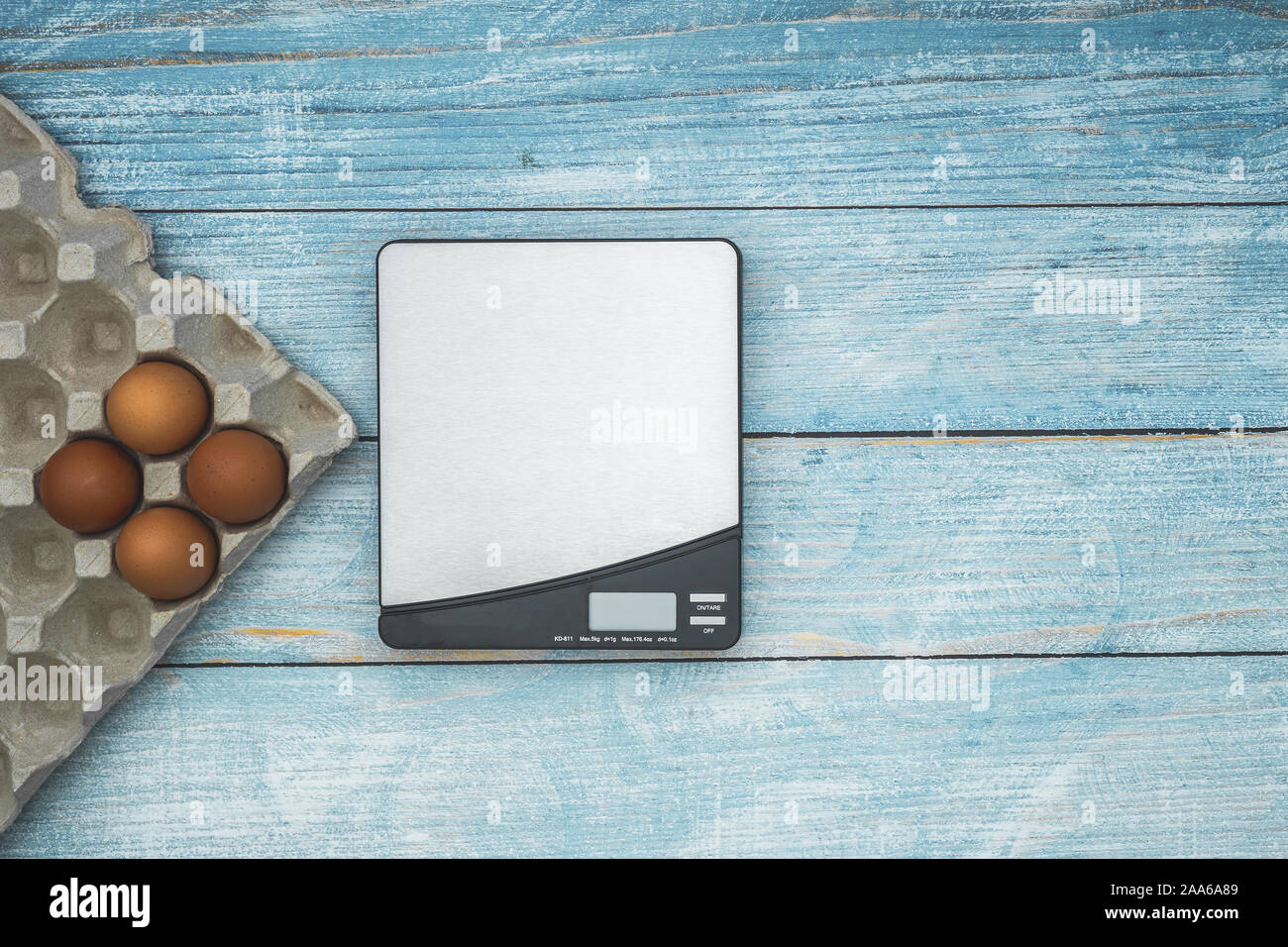 Electronic weighing scale and four raw eggs flat lay on rustic blue