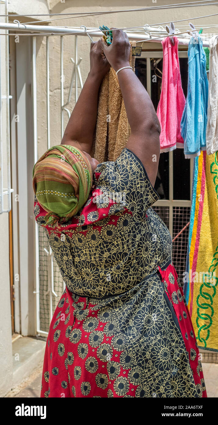 Alberton, South Africa - unidentified black African woman hangs laundry out to dry on a washing line outdoors image in vertical format Stock Photo