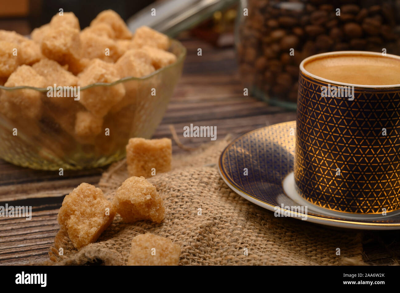 Pieces of brown sugar in a sugar bowl, a Cup of coffee, coffee beans on a wooden background. Close up Stock Photo