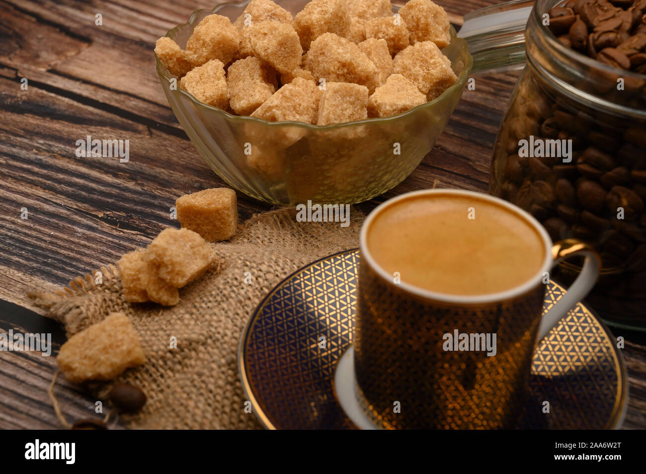 A Cup of coffee, pieces of brown sugar in a sugar bowl, coffee beans in a glass jar on a wooden background Stock Photo