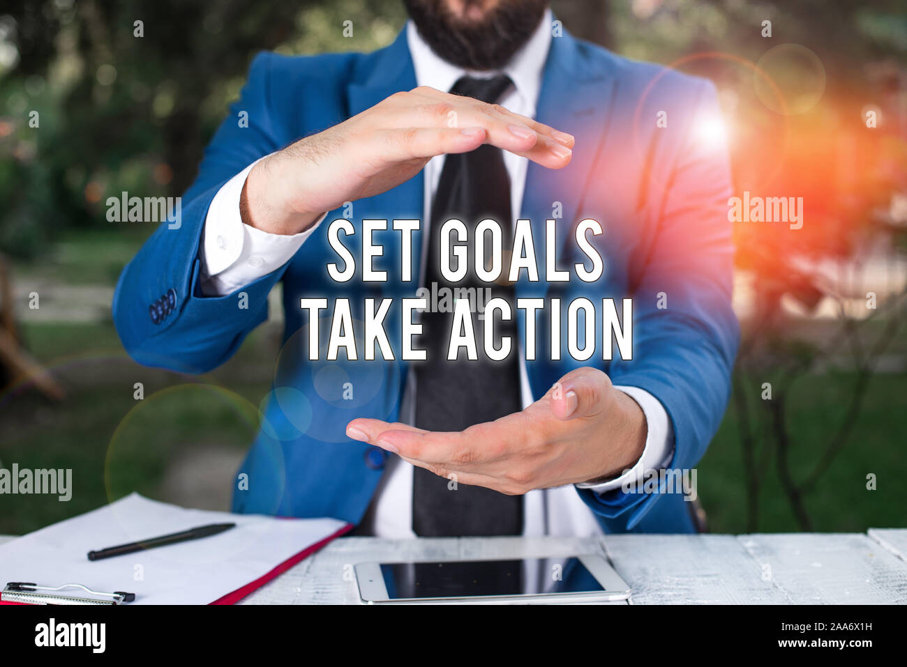 Conceptual hand writing showing Set Goals Take Action. Concept meaning Act on a specific and clearly laid out plans Man in front of table. Mobile phon Stock Photo
