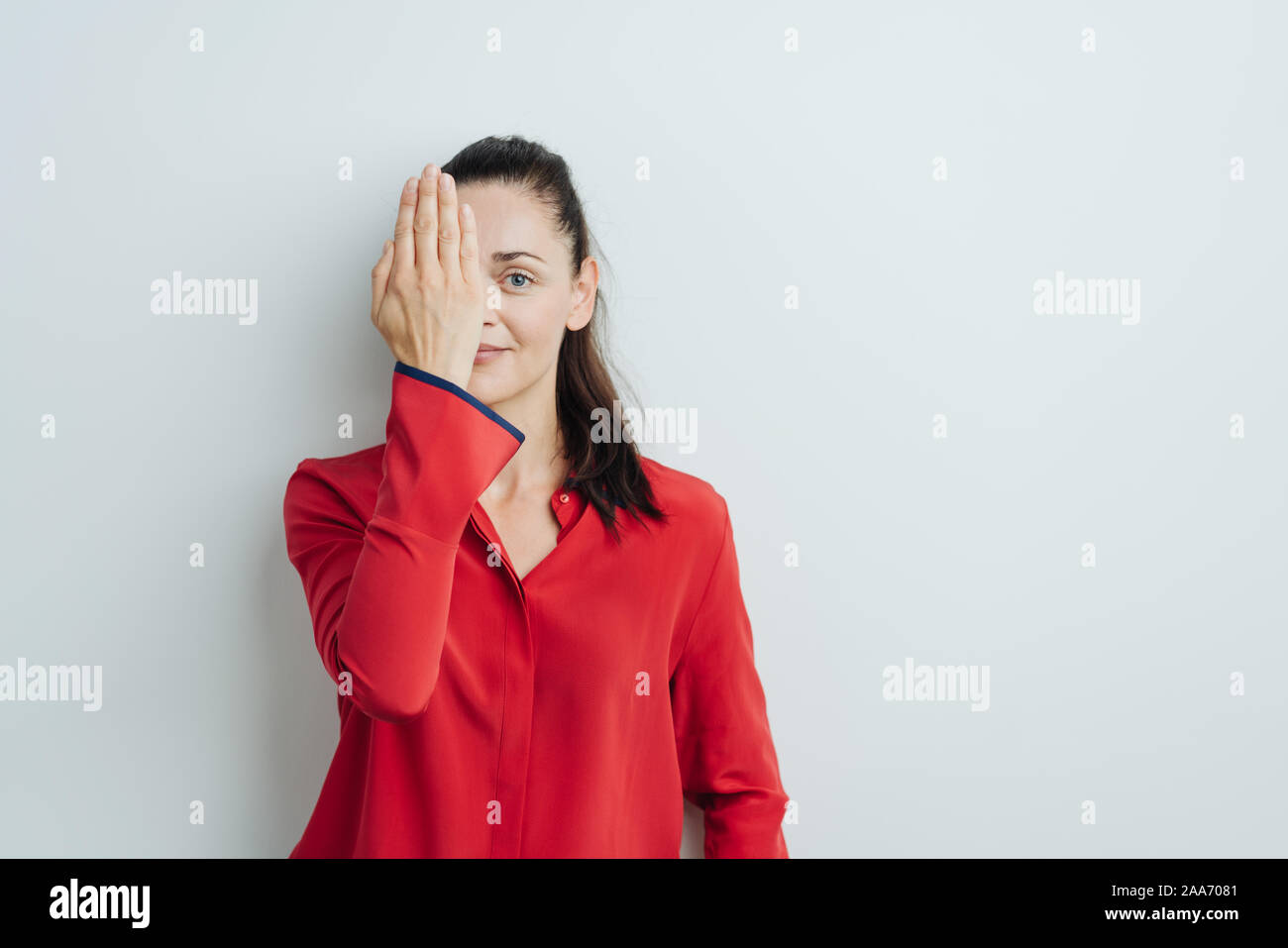 Smiling young woman covering one eye with her hand as she looks at