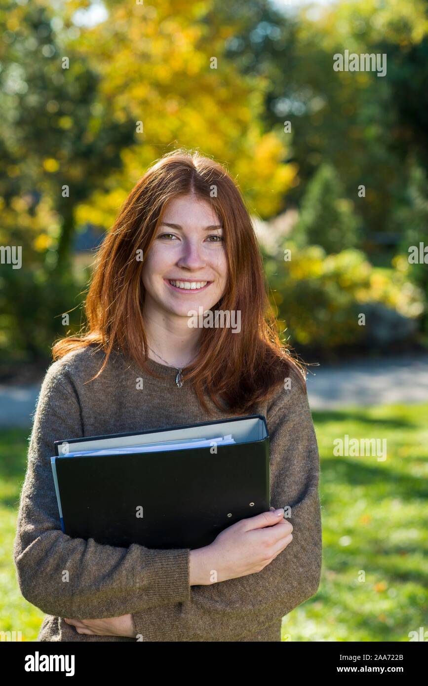 Young smiling red-haired woman, student, pupil holds folder, Bavaria, Germany Stock Photo