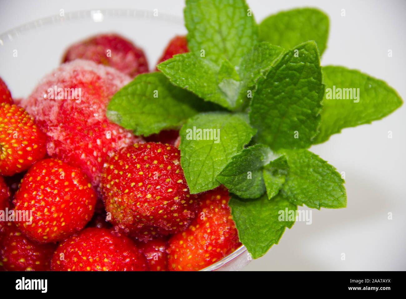 frozen strawberries with mint leaves in a glass on a white background ...