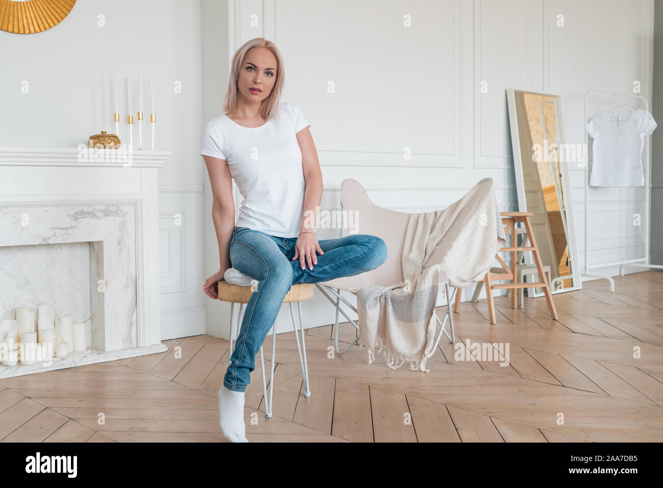 Beautiful young girl posing sitting on a chair in casual clothes in a bright room Stock Photo