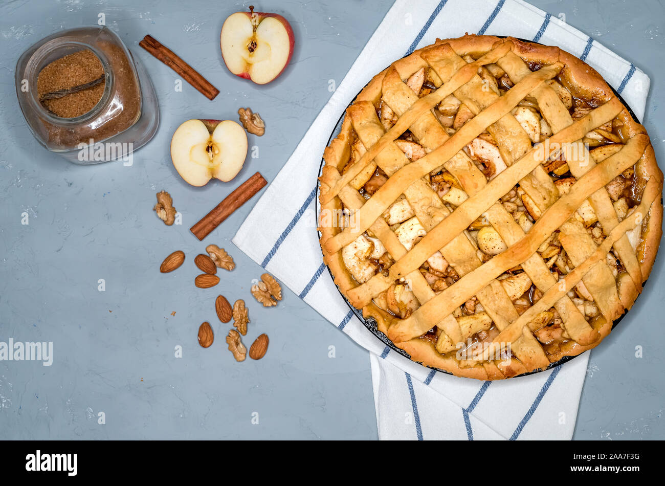 apple pie on a gray kitchen towel, with apples, cinnamon, sugar and nuts, top view Stock Photo