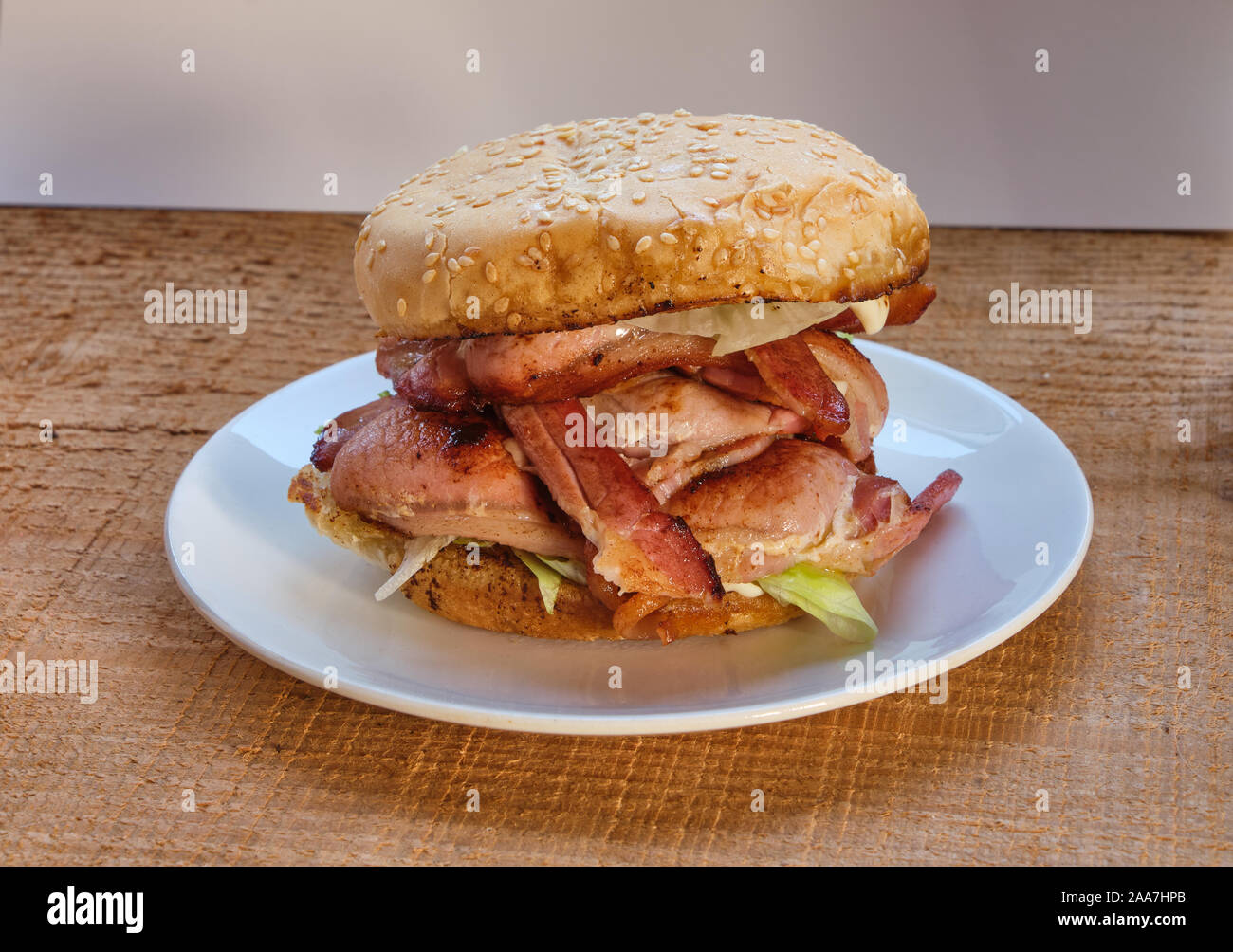 Bacon roll or butty with lettuce on a white plate and wooden board in a sesame coated roll or bap Stock Photo
