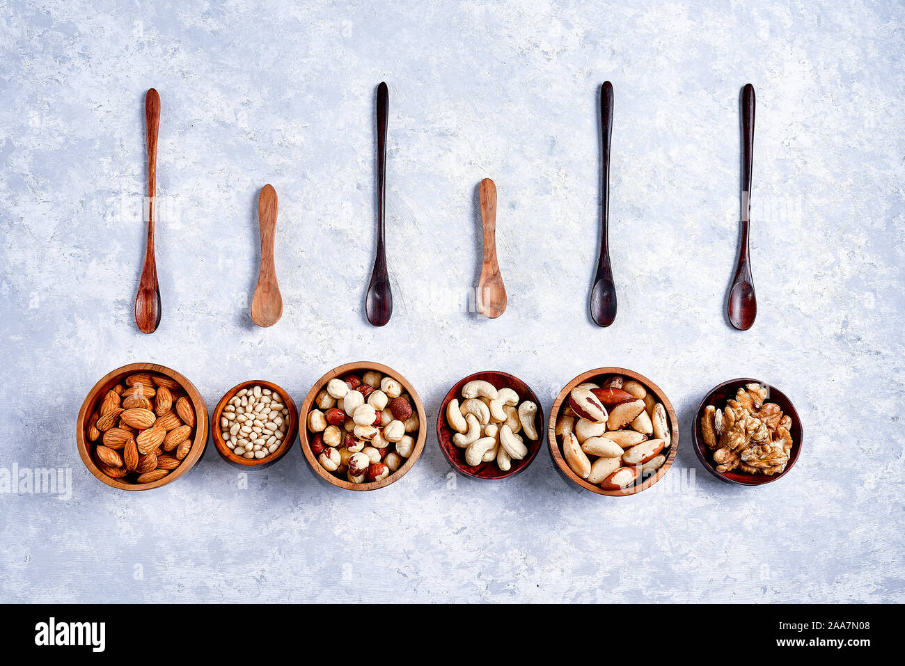 pecans, hazelnuts, almonds, pine nuts, cashews in wooden bowls on blue background, top view Stock Photo
