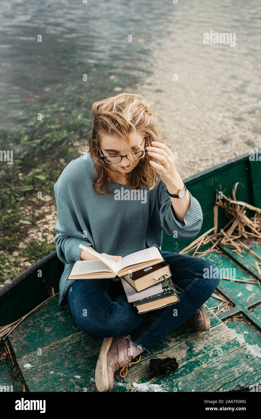 Portrait of young beautiful woman sitting on a boat and reading a book. She is bookworm and she choose between few books. Stock Photo