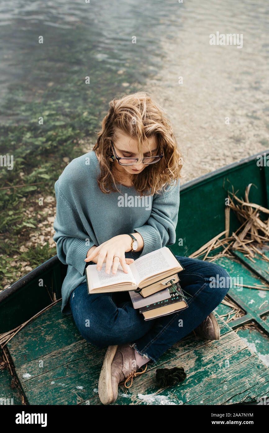 Portrait of young beautiful woman sitting on a boat and reading a book. She is bookworm and she choose between few books. Stock Photo