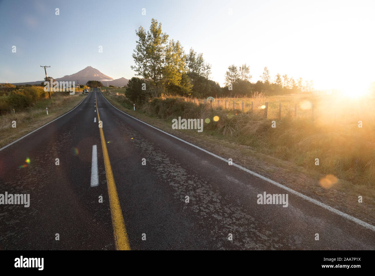 Wide angle view on Mount Taranaki (Mount Egmont) in New Zealand with road leading to it. Taken during sunset with sun rays and lens flare visible. Stock Photo