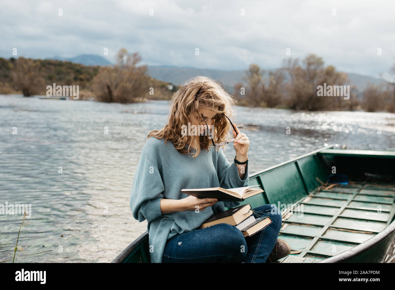 Portrait of young beautiful woman sitting on a boat and reading a book. She is bookworm and she choose between few books. Stock Photo