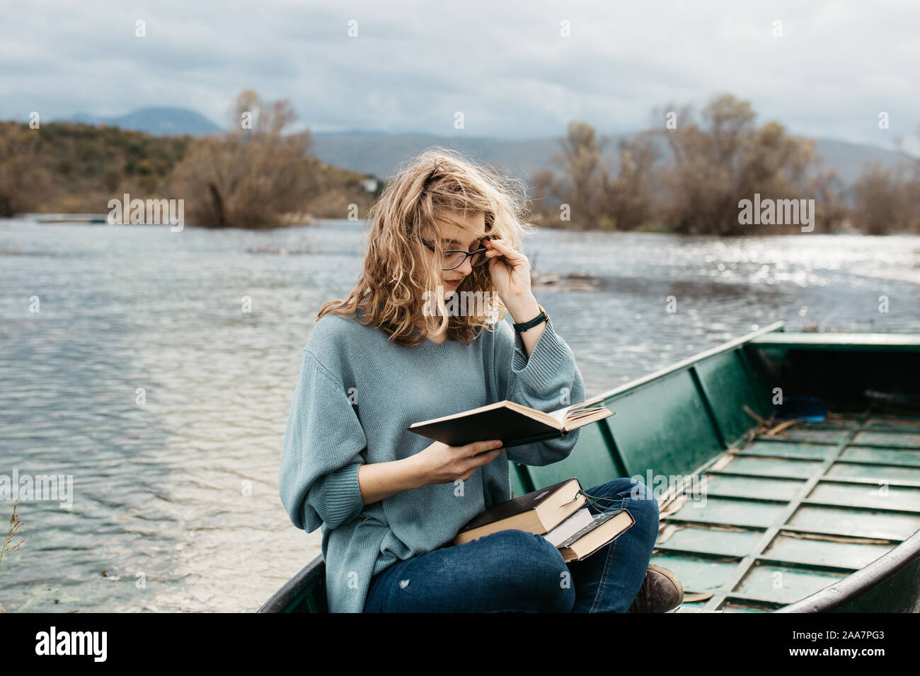 Portrait of young beautiful woman sitting on a boat and reading a book. She is bookworm and she choose between few books. Stock Photo