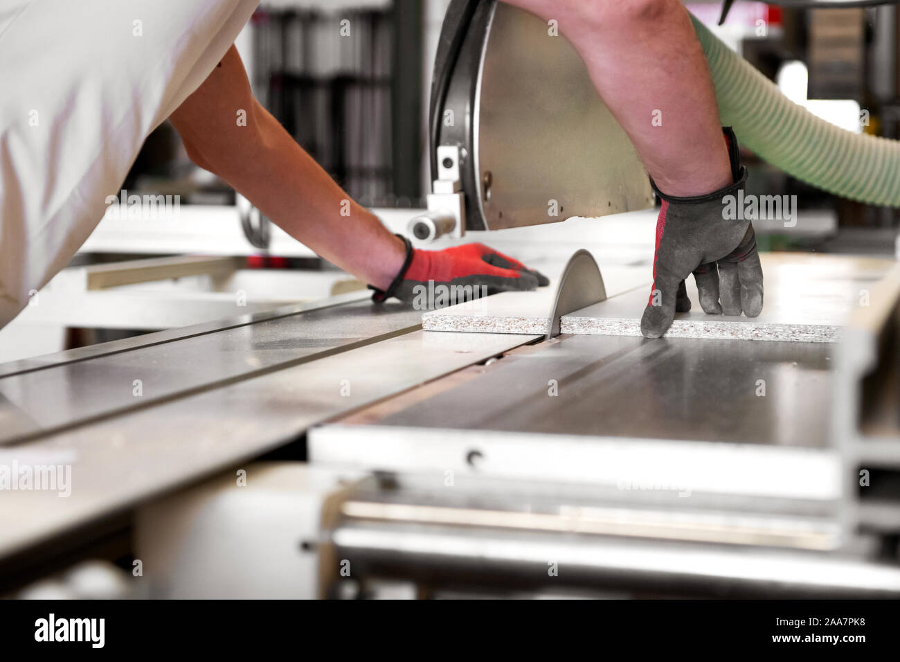 Carpenter cutting a wooden panel on a circular saw in a workshop viewed low angle from his perspective with focus to the blade and his hands Stock Photo