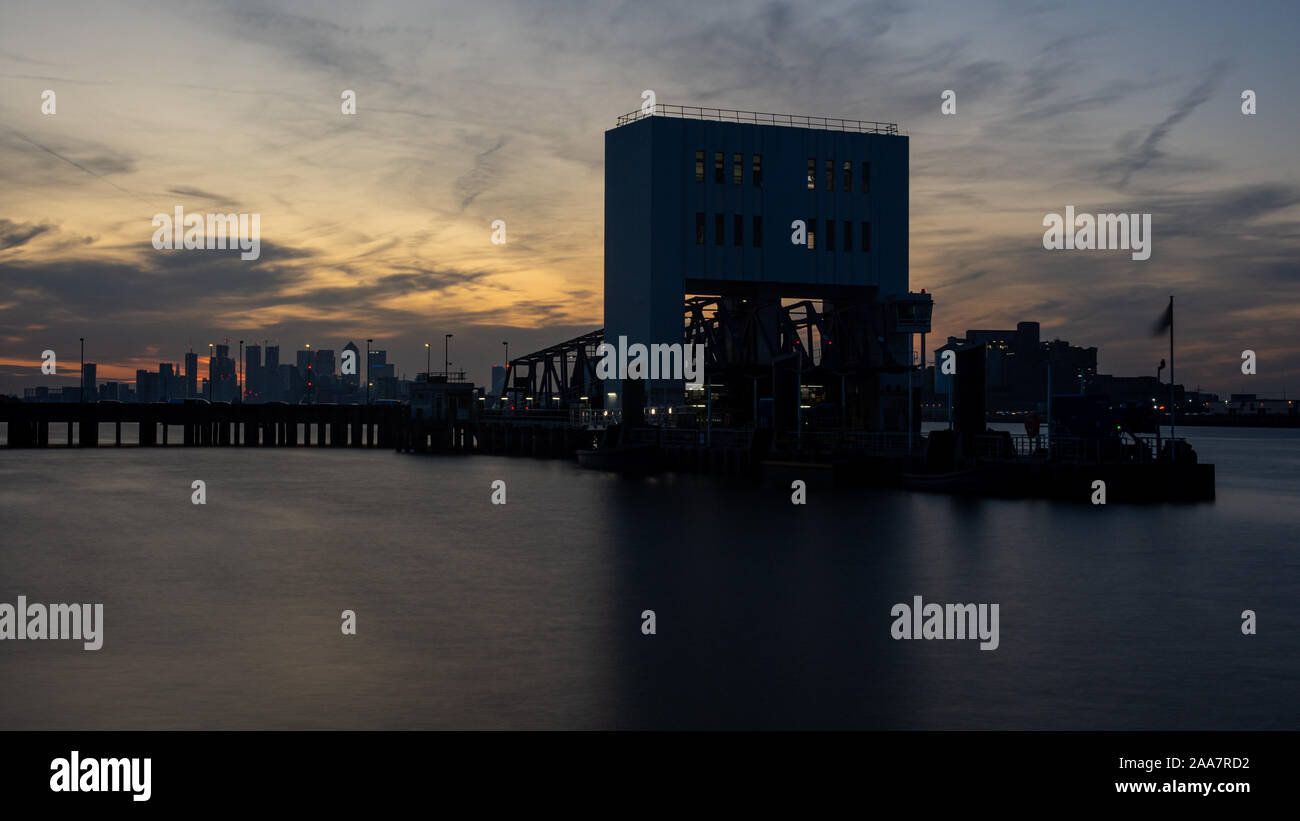 London, England, UK - September 21, 2019: The sun sets behind Woolwich's ferry pier, with the skyline of London's Docklands in the distance. Stock Photo