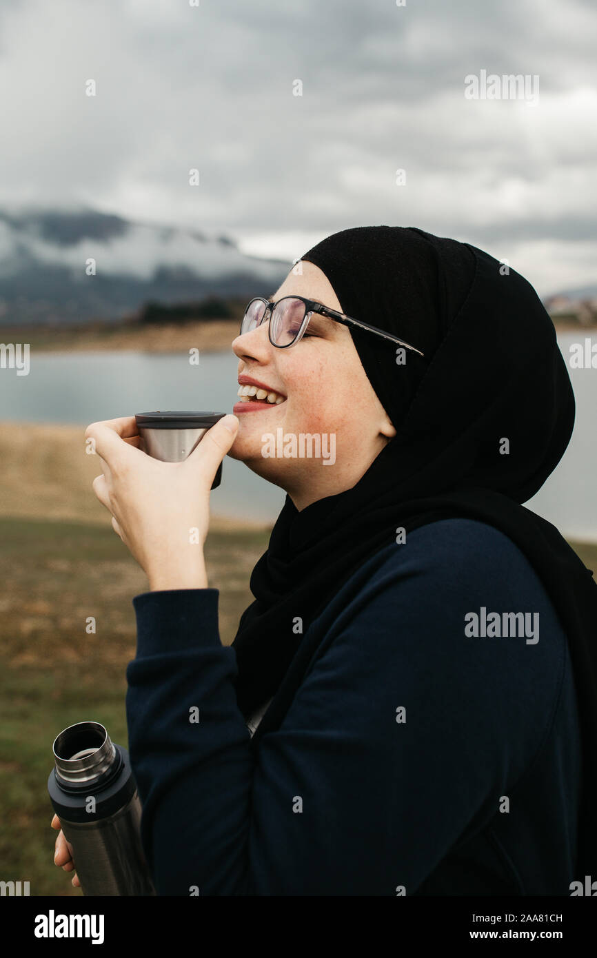 Happy woman with hijab drinking coffee in nature, on a foggy morning ...