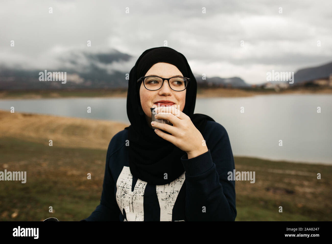 Happy woman with hijab drinking coffee in nature, on a foggy morning ...