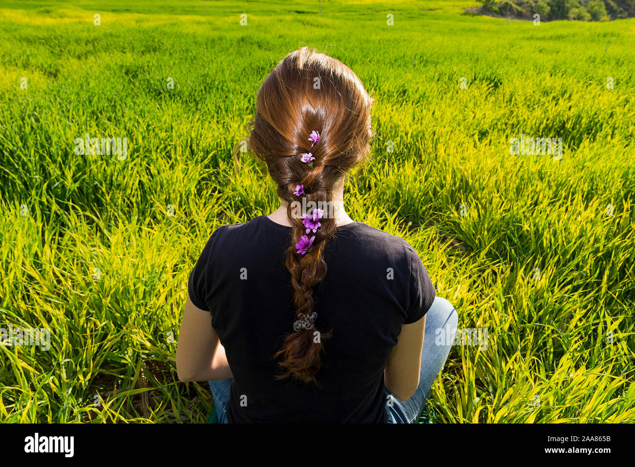 Young caucasian woman red-haired with freckles, resting on a green field at spring sunset, sitting in a yoga position. Meditation, mindfulness, relax Stock Photo