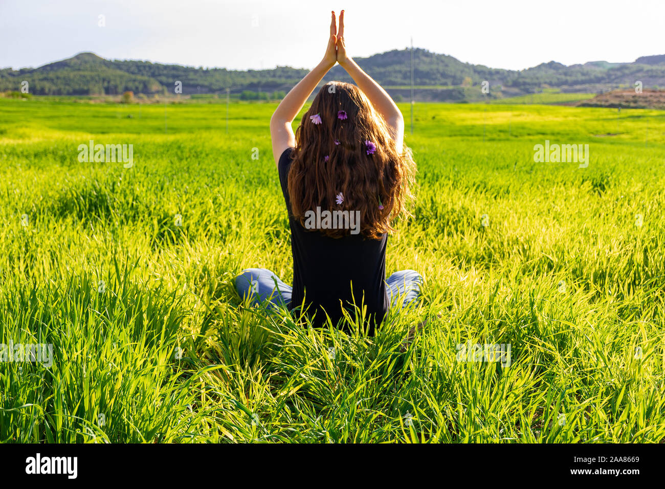 Young caucasian woman red-haired with freckles, resting on a green field at spring sunset, sitting in a yoga position. Meditation, mindfulness, relax Stock Photo