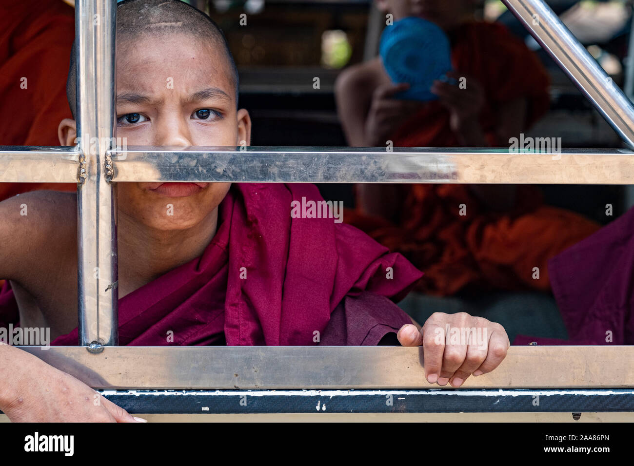 A young Buddhist monk dressed in a scarlet robe peers out through window slats from the back of a local jitney in Bagan (Pagan), Myanmar (Burma) Stock Photo