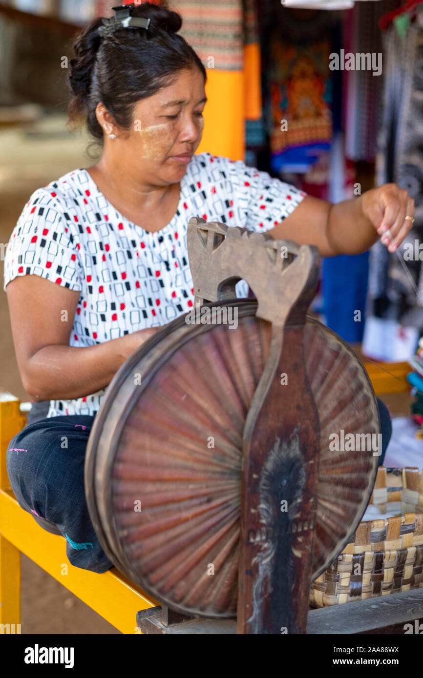 Older Burmese female weaver uses a spinning wheel to create thread for weaving traditional fabrics of the Bagan (Pagan) region of Myanmar (Burma) Stock Photo