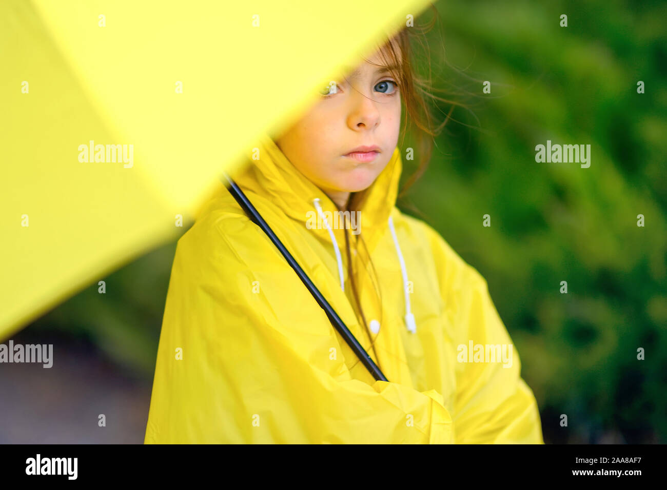 cute little girl in a yellow raincoat is hiding from the rain under an  umbrella Stock Photo - Alamy
