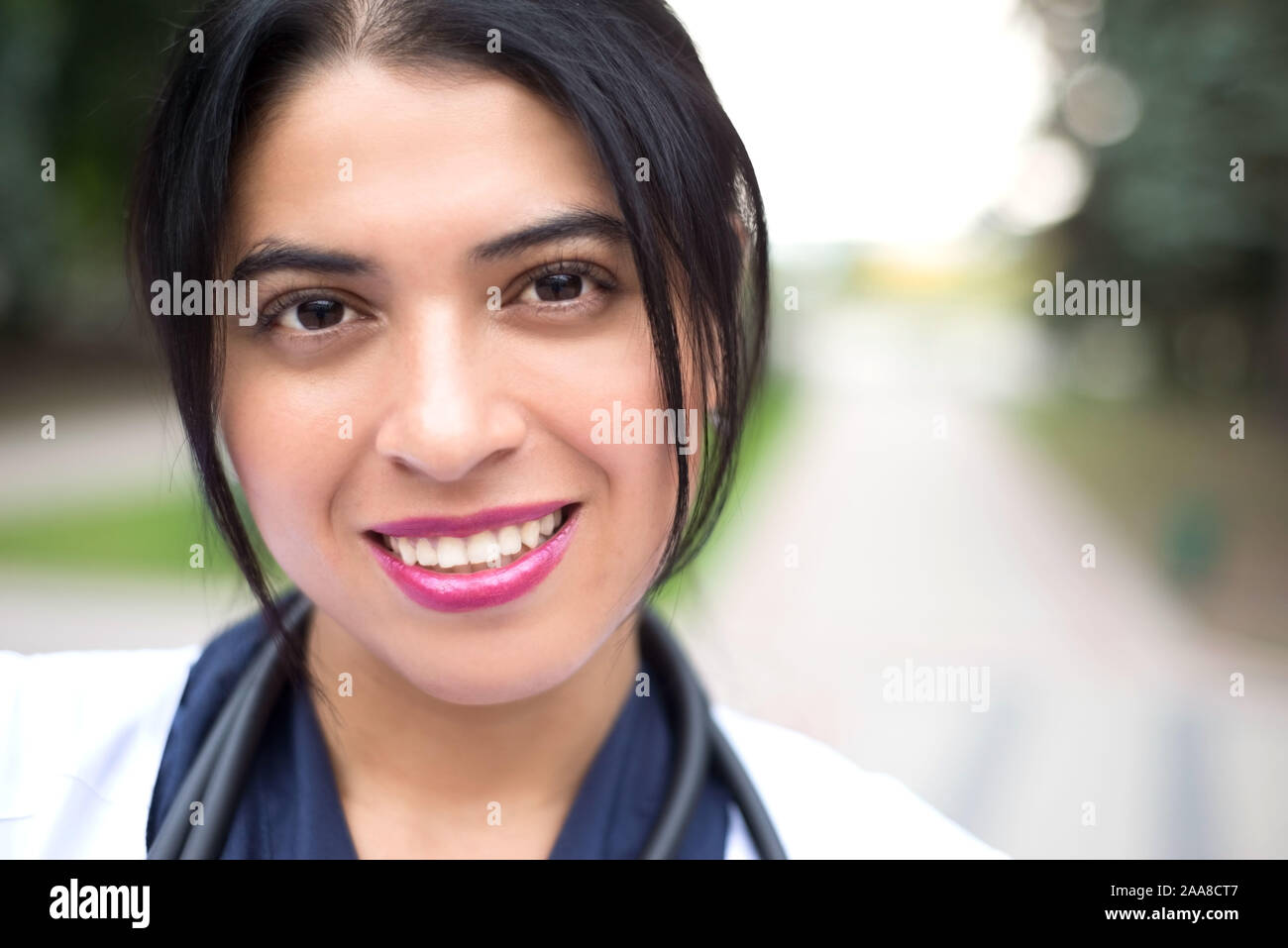 portrait of a beautiful, young mexican girl doctor. Smiles. Woman in a white coat with a stethoscope. Outdoor in Stock Photo