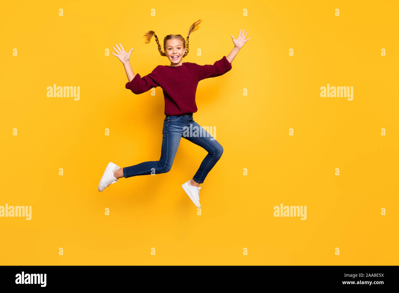 Full length body size photo of cheerful positive excited gitl in jeans denim burgundy sweater jumping up footwear isolated vivid color background Stock Photo