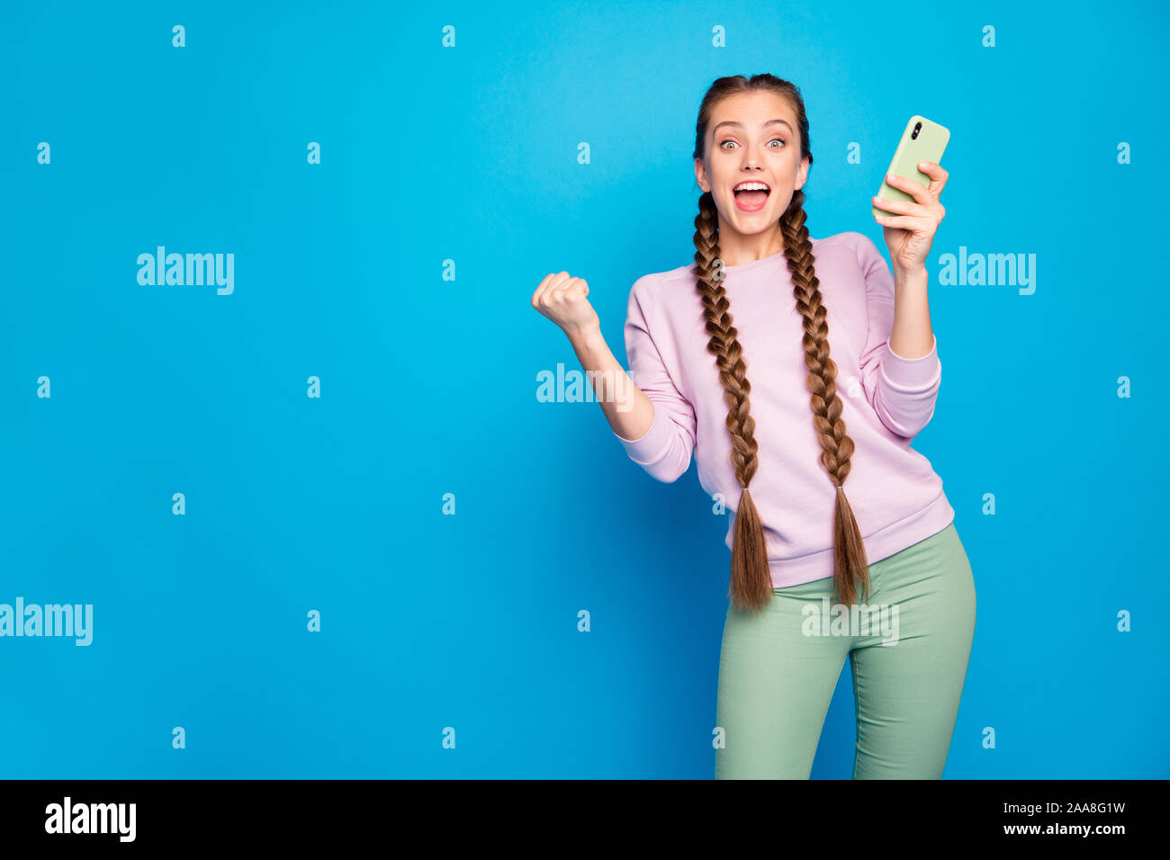 Portrait of delighted sweet youngster girl blogger use smartphone get social network like notification raise fists scream omg wow wear pullover green Stock Photo