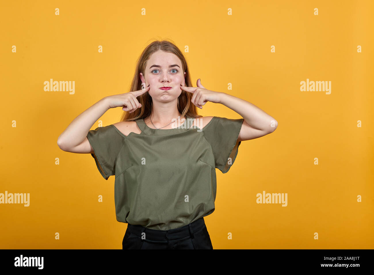 Young funny lady wearing nice shirt puffing cheeks and keeping fingers Stock Photo