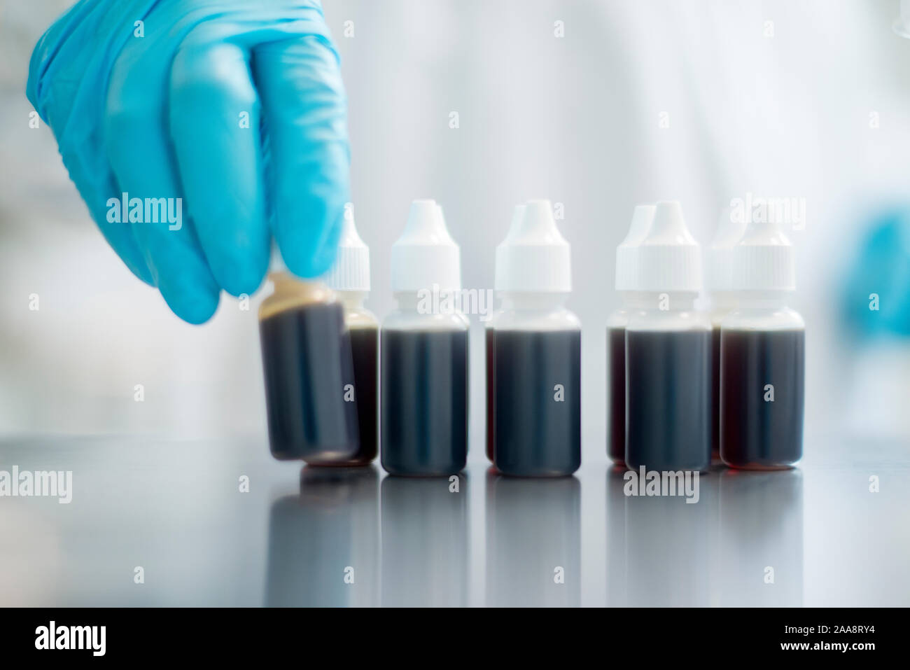 Blue glove hand picking up a vile with dark liquid Stock Photo