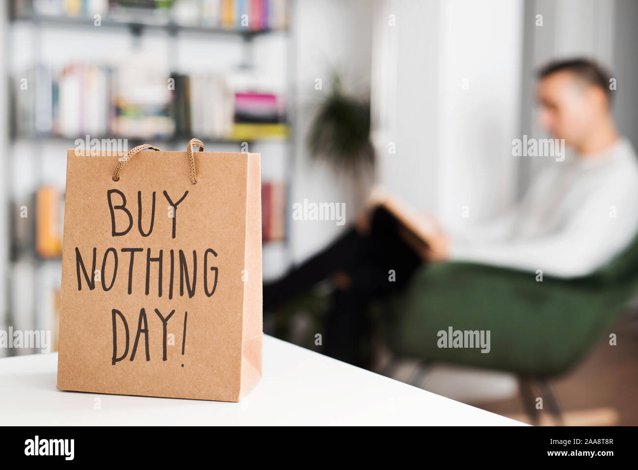 closeup of a shopping paper bag, with the text buy nothing day written in it, and a man reading a book sitting in a modern rocking chair in the backgr Stock Photo