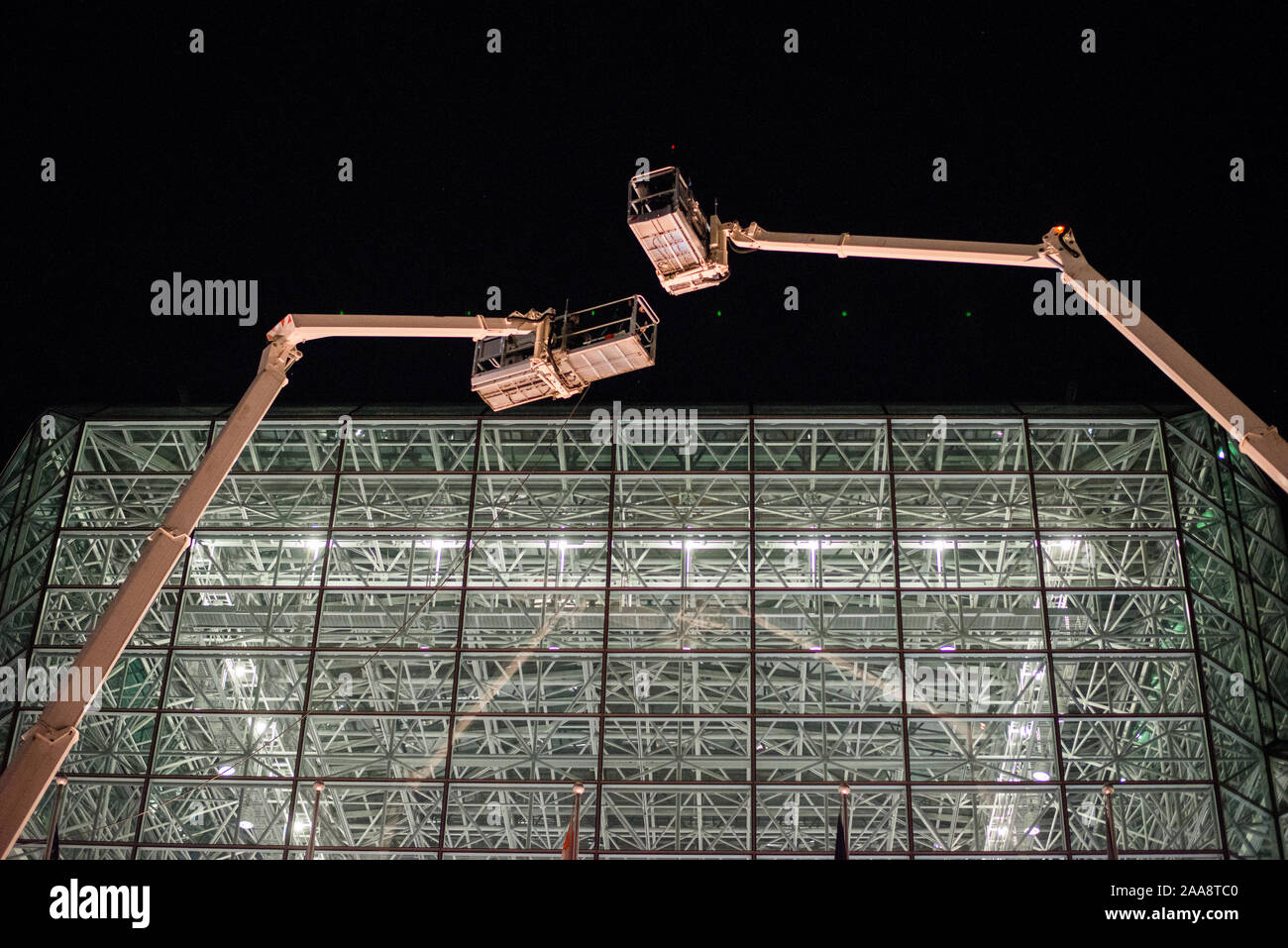 Two cranes hover over glass structure at night Stock Photo