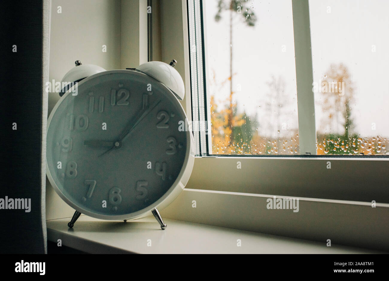 a large alarm clock on a window ledge with rain on the window Stock