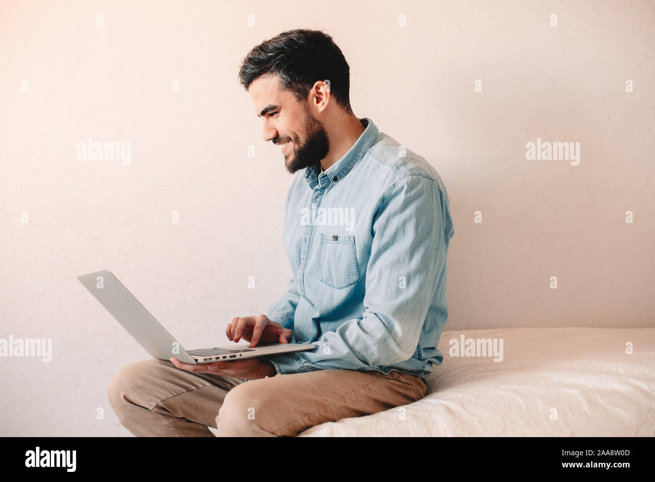 Happy man using laptop computer while sitting at home against wall Stock Photo