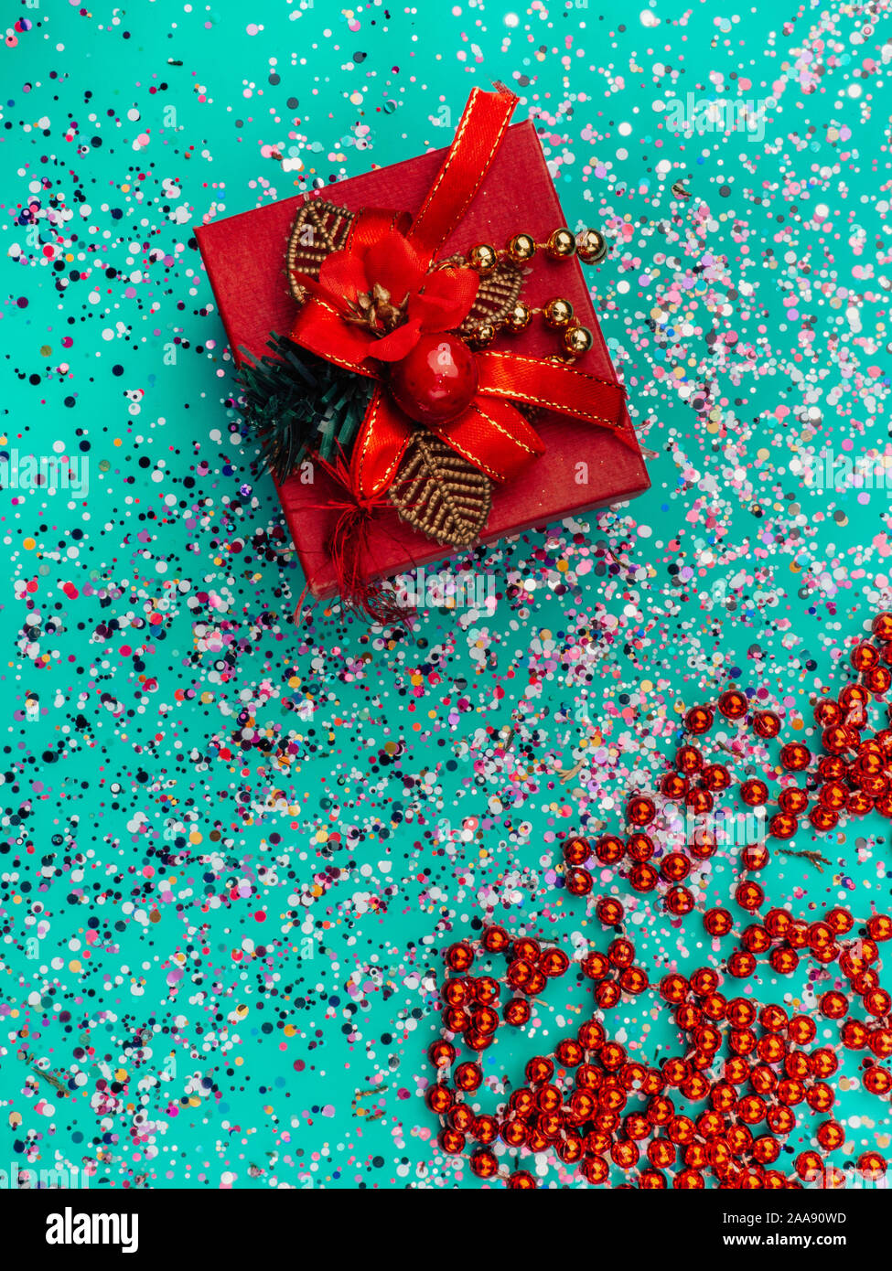 Red gift box with red decoration on turquoise background with colorful glitter, cones. Holiday concept. Topo view Stock Photo