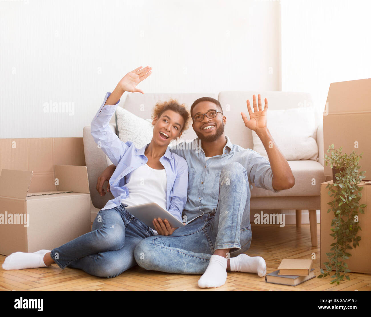 Spouses Using Tablet Sitting Among Moving Boxes Discussing Renovation Indoor Stock Photo
