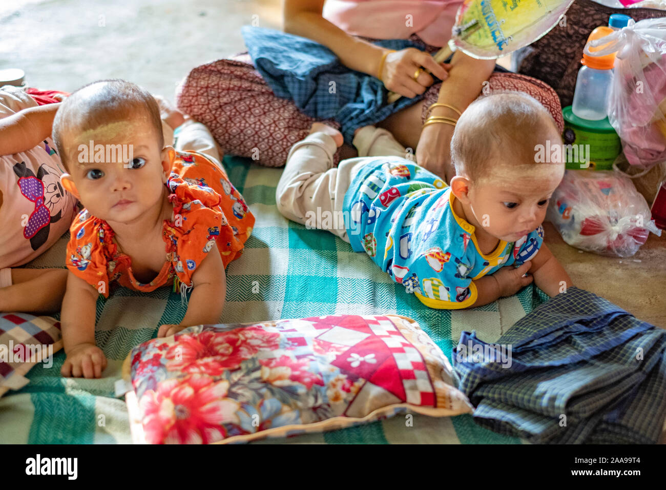 Twin Burmese babies romp on the floor of their mother's market stall in rural Myanmar (Burma) with sun protecting powder on their faces Stock Photo