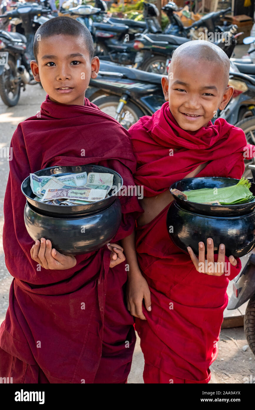 Two young Buddhist monks with offering bowls filled with offerings and money and dressed in brilliant red robes with innocent smiles Stock Photo