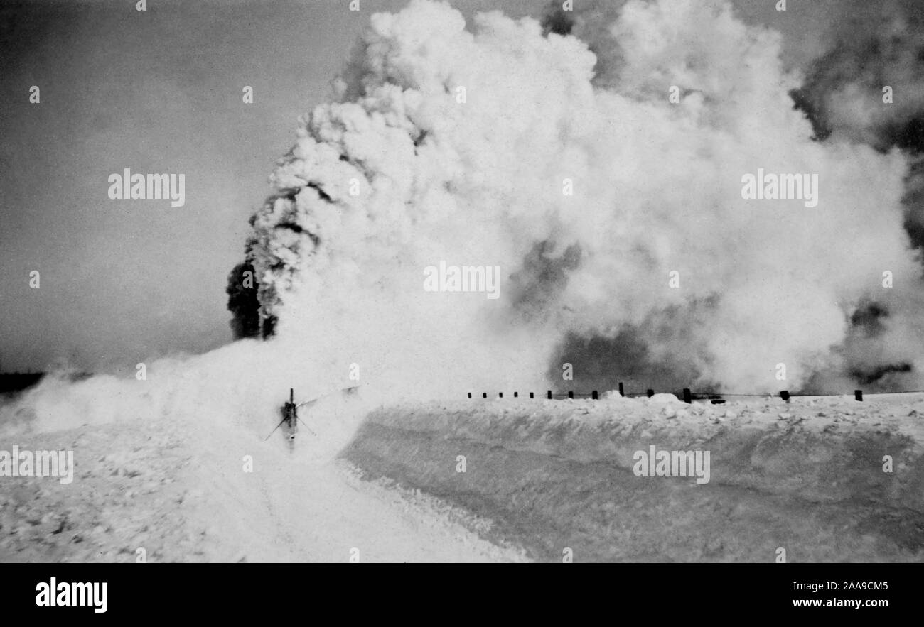 A locomotive fitted with a snow plow bursts through a drift along some railroad tracks in South Dakota, ca. 1925. Stock Photo