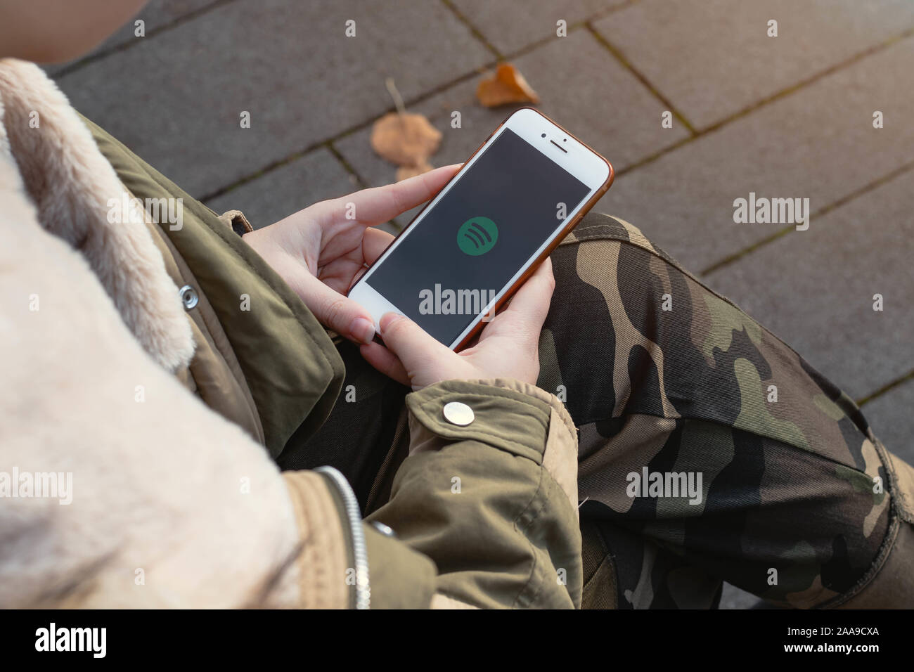 Woman holding a phone in the hands. Spotify logo on the cellphone screen. Stock Photo
