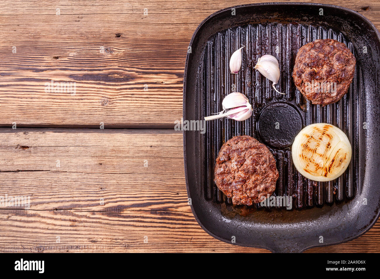 Fried burger beef cutlets with onion, garlic on grill pan on wooden background Stock Photo