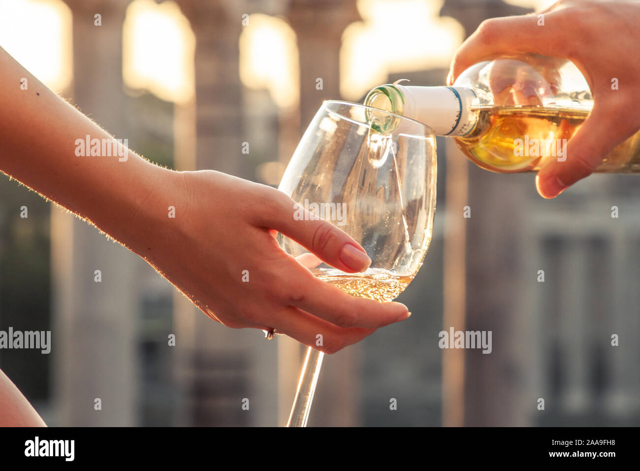 Pouring bottle of white wine in glasses at Roman Forum at sunrise. Historical imperial Foro Romano in Rome, Italy from panoramic point of view. Stock Photo