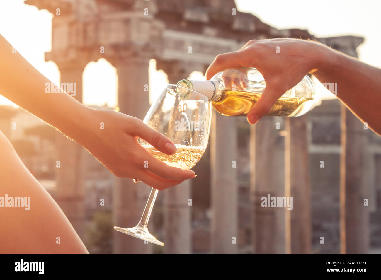 Pouring bottle of white wine in glasses at Roman Forum at sunrise. Historical imperial Foro Romano in Rome, Italy from panoramic point of view. Stock Photo